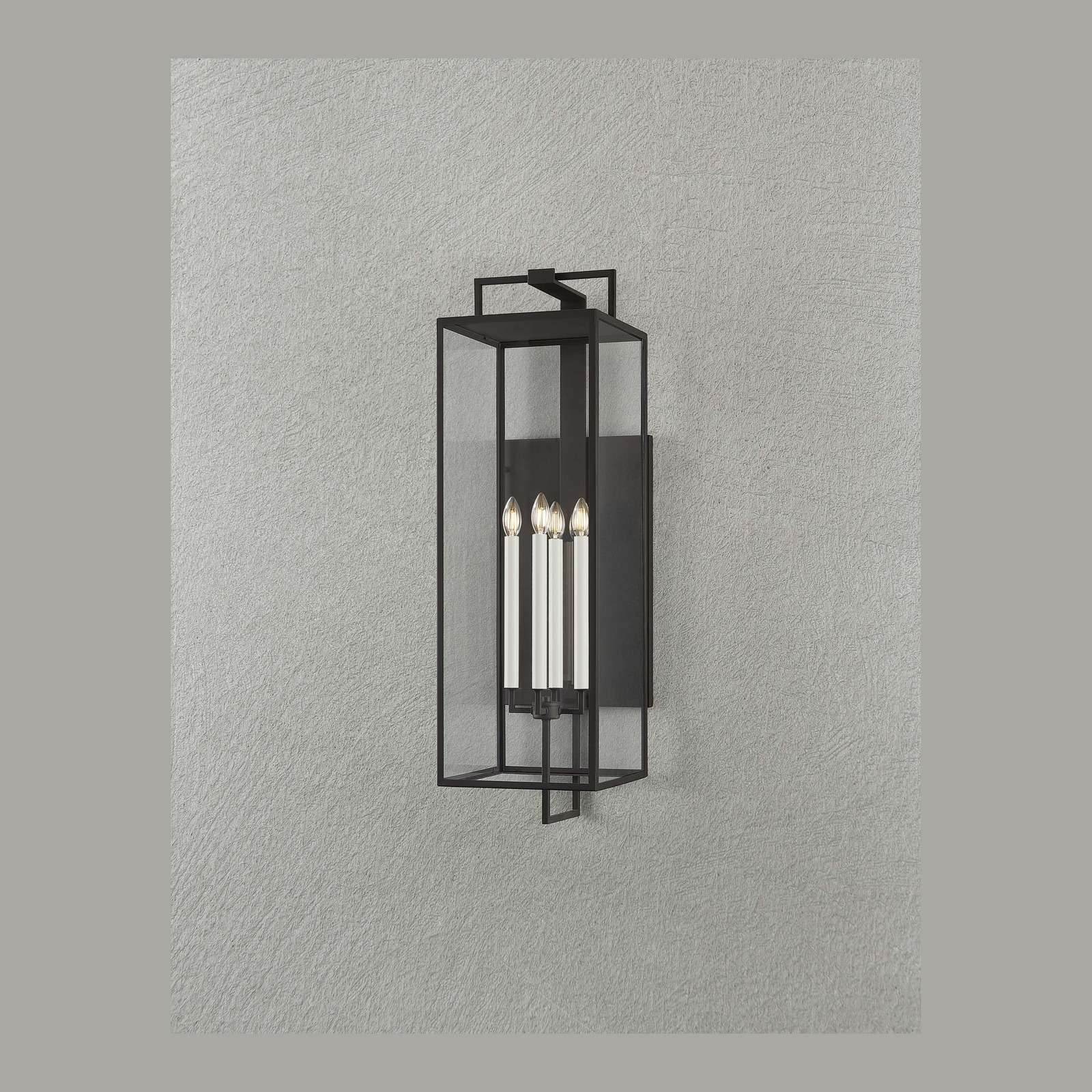 Black forged iron clear glass outdoor wall lantern sconce mounted on a white exterior patio wall with black framed doors and windows.