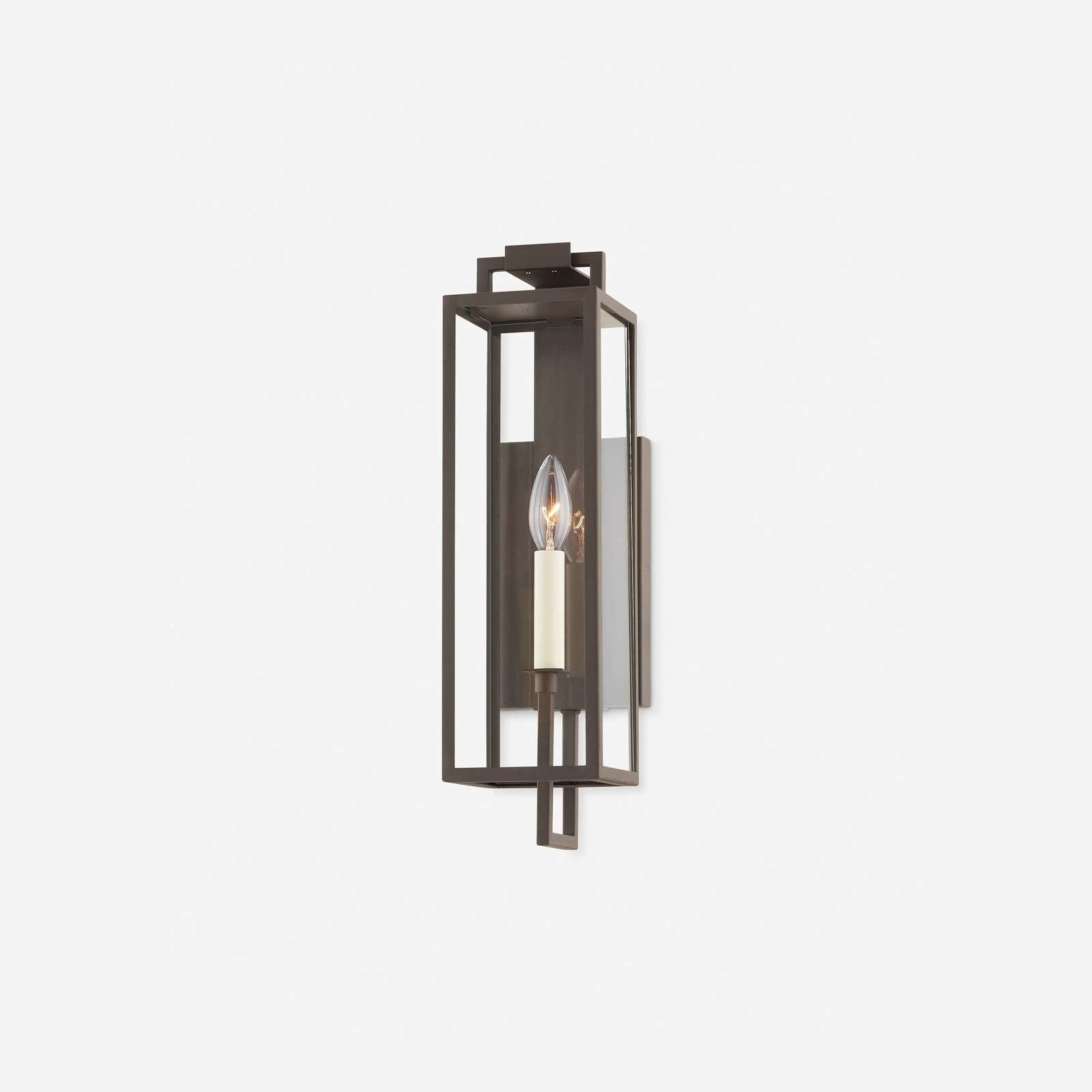 Black forged iron clear glass outdoor wall lantern sconce mounted on a white exterior patio wall with black framed doors and windows.