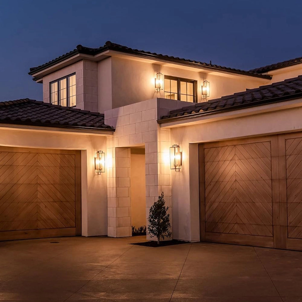 Black forged iron clear glass outdoor wall lantern sconce mounted on a white exterior patio wall with black framed doors and windows.
