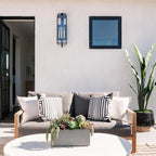 Black forged iron clear glass outdoor wall lantern sconce mounted on a white exterior patio wall with black framed doors and windows.